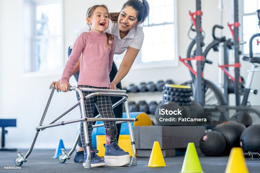 A little girl with a limb difference and a leg brace works with her physical therapist as she learns to use a walker